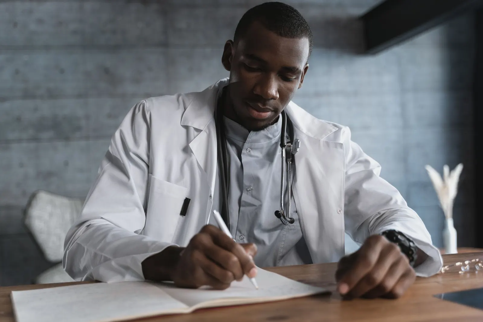 Doctor in a white coat writing notes at his consulting-room desk